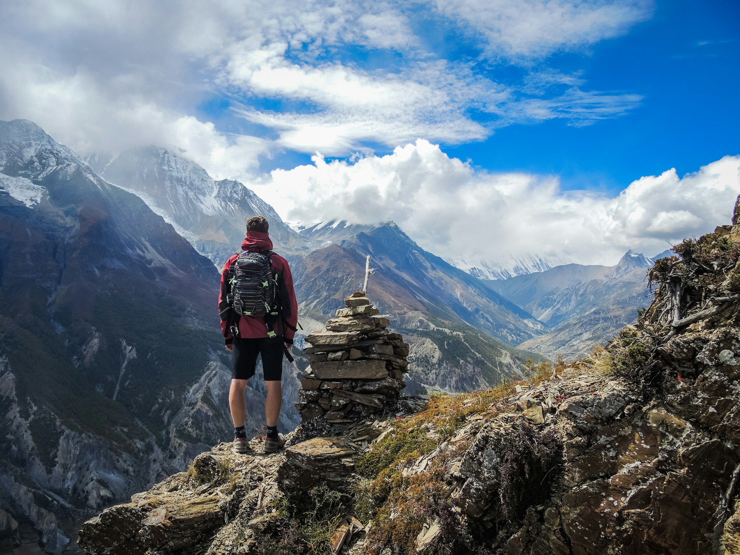 Hiker standing above a Himalayan valley near a stone cairn