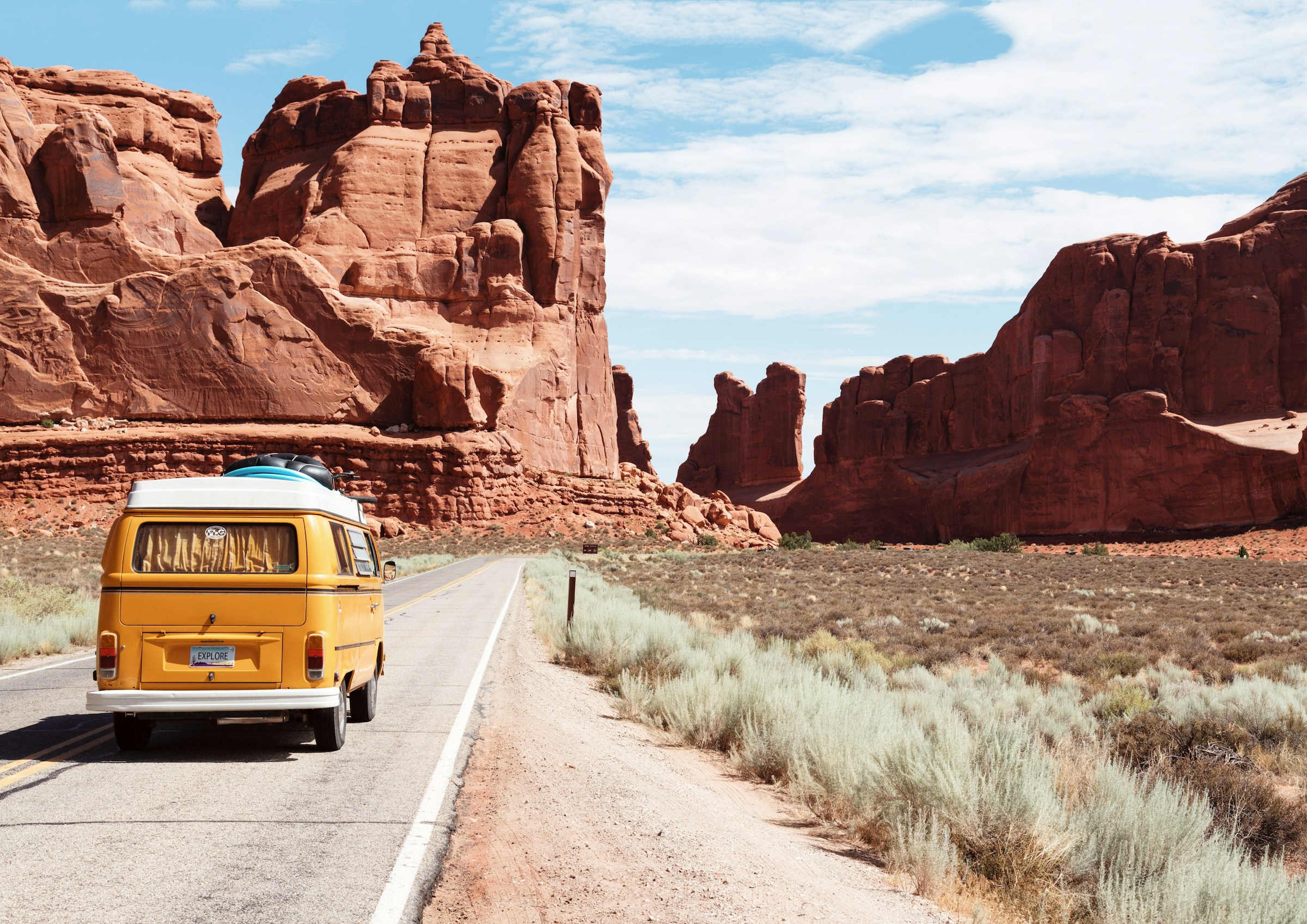 Yellow camper van driving between red rock formations
